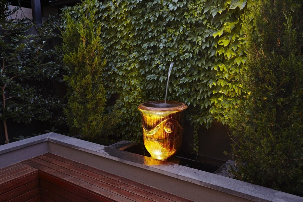 Lit urn water feature at dusk against a planted wall
